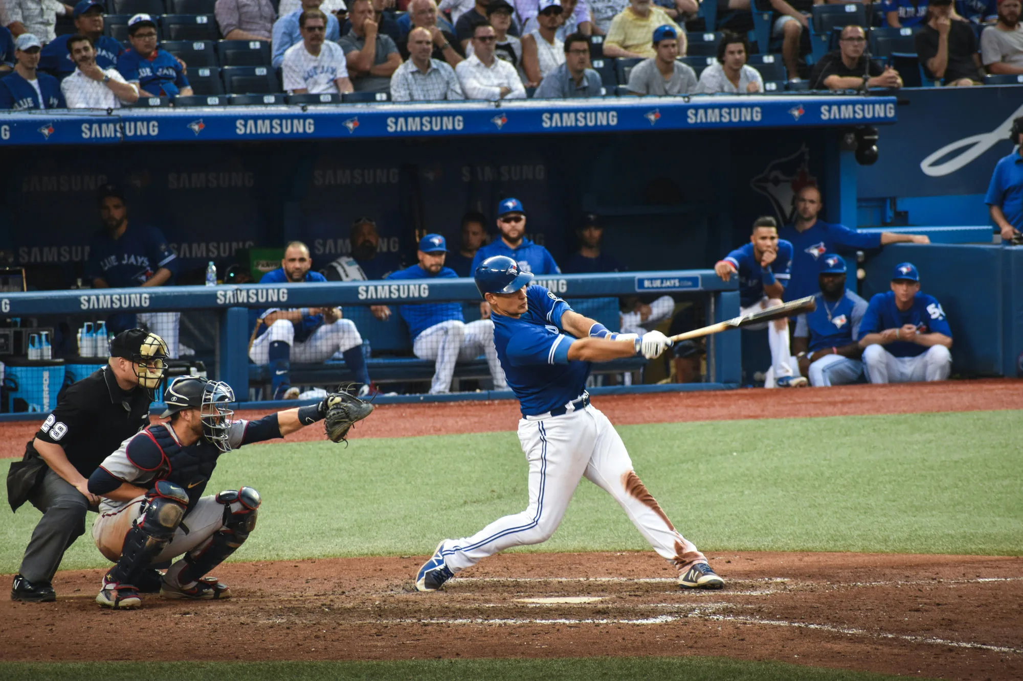 A baseball batter follows through on a swing in front of a packed stadium.